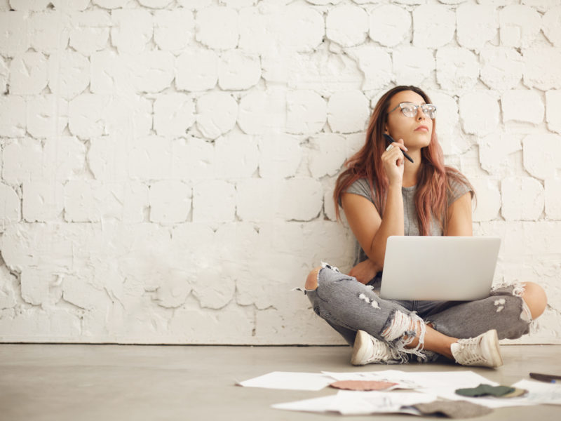 photo of young woman thinking and writing on laptop