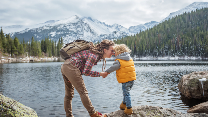 photo of a mother and son hikers in front a lake with mountains and evergreen trees in the background
