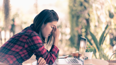 photo of frustrated woman holding her face while sitting at a laptop outside