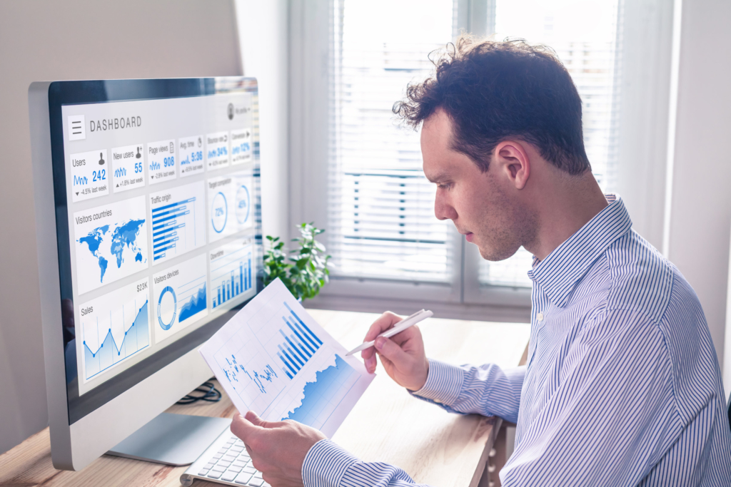 photo of man studying analytics at his desk, computer with charts on screen
