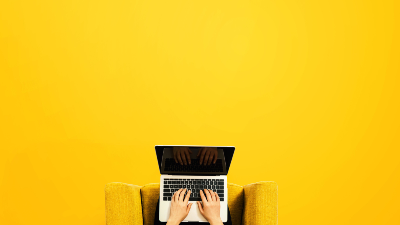 photo of seated person on laptop with yellow minimalist background