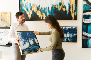 Male artist showing his painting to a female client interested in buying some artwork from the exhibition of the art gallery