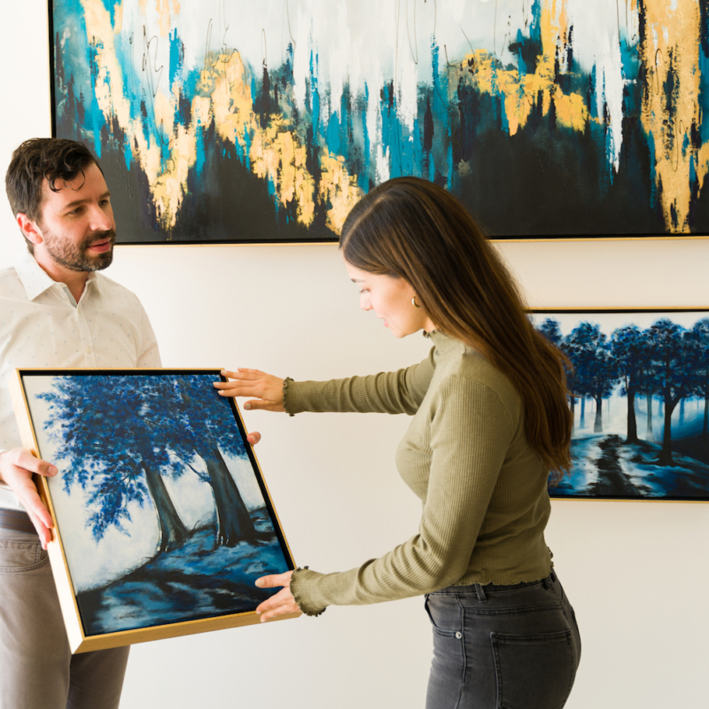 Male artist showing his painting to a female client interested in buying some artwork from the exihibiton of the art gallery