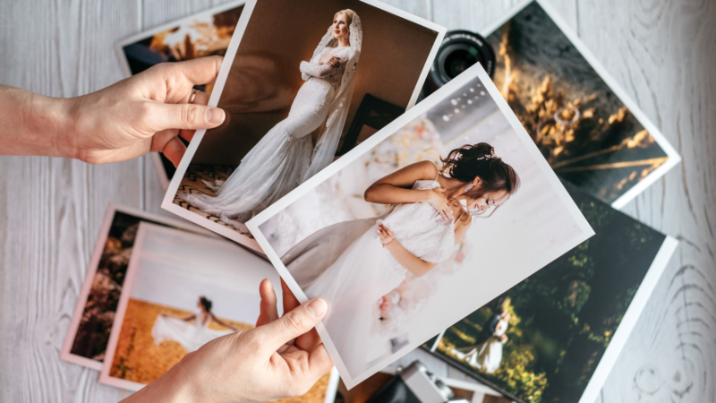 Person holding two printed photos of brides over stack of other wedding photos