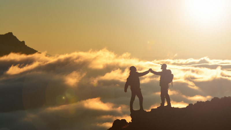 two climbers on a mountaintop - success, teamwork, positive mindset concept