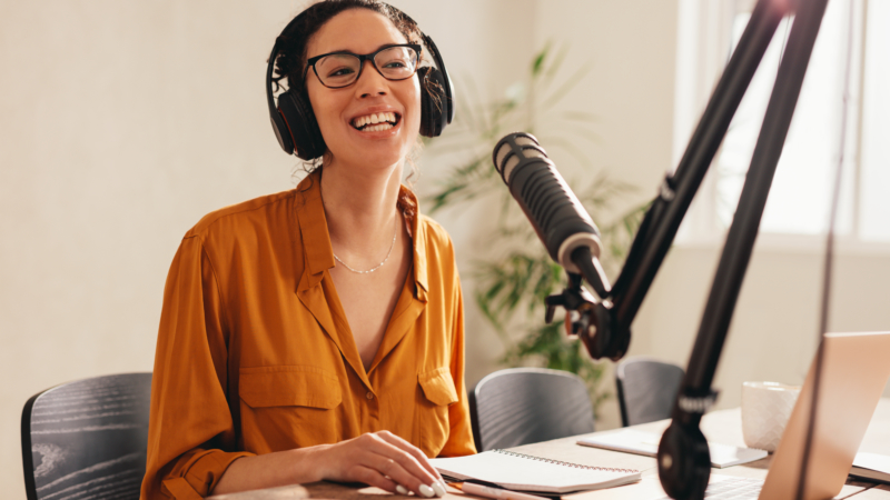 female podcaster smiling, wearing headphones in front of mic