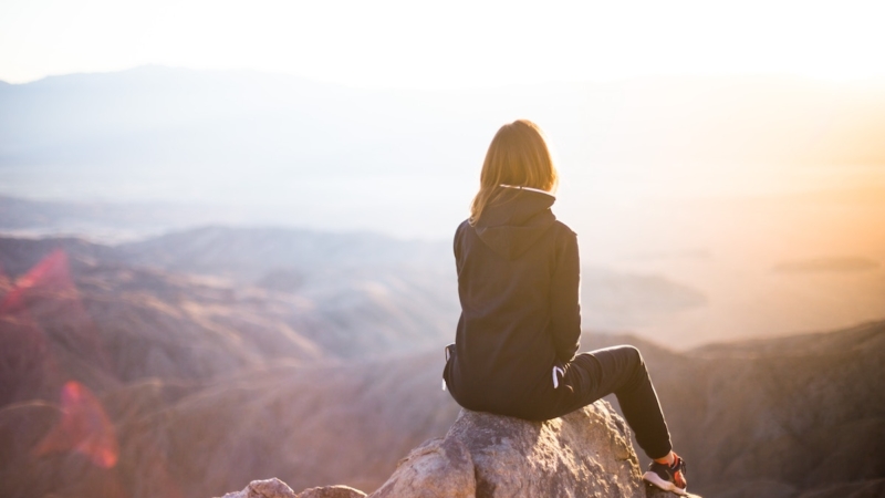 woman sitting on mountain peak looking out at sky