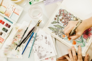 person using paints and pen to create floral artwork