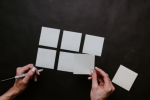 person laying out white note paper out on a black background in shape of a grid