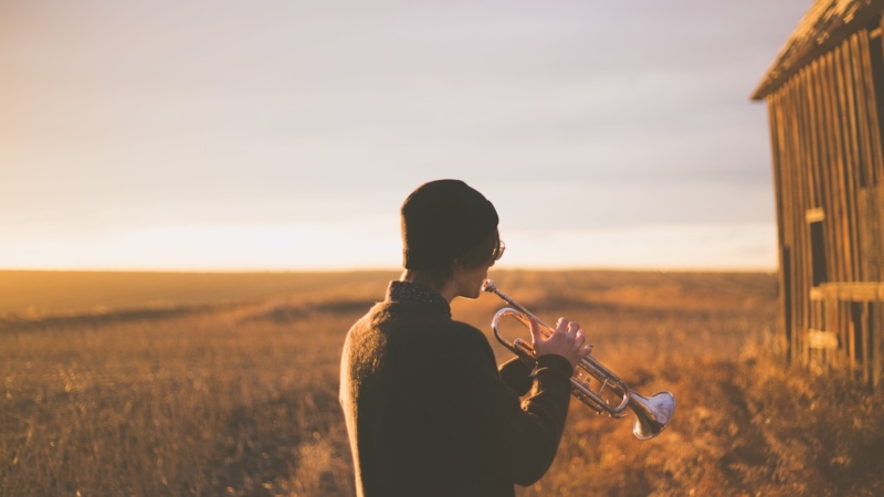 man playing trumpet outside house on field during daytime
