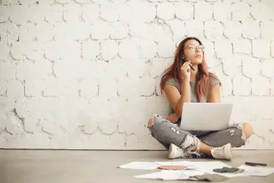 photo of young woman thinking and writing on laptop