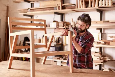 Main working on handmade chair in woodworking shop