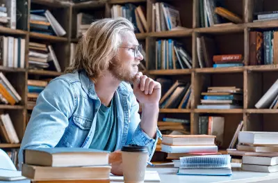 Man sitting in library with books around him looking off and thinking
