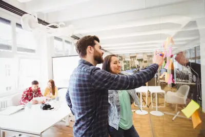 Smiling business people looking at sticky notes on glass in meeting room at creative office
