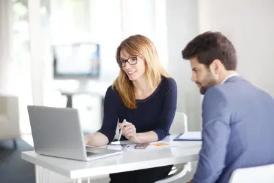 Investment Advisor Businesswoman Sitting At Office Desk With Client Looking at Laptop
