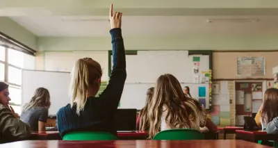 Back view of classroom, girl raising hand with question