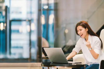 Beautiful Asian girl celebrate with laptop, success happy pose. E-commerce, university education, internet technology, or startup small business concept. Modern office or living room with copy space