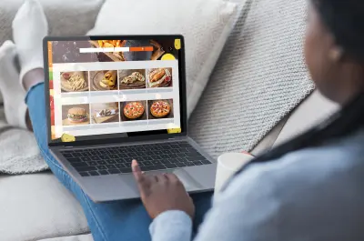 Black Woman Using Laptop Ordering Fast food Meals Online On Restaurant Website Sitting On Sofa At Home. 