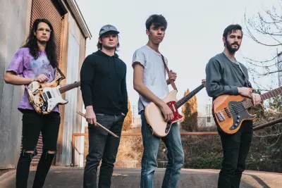 four person band holding musical instruments standing near brown metal door
