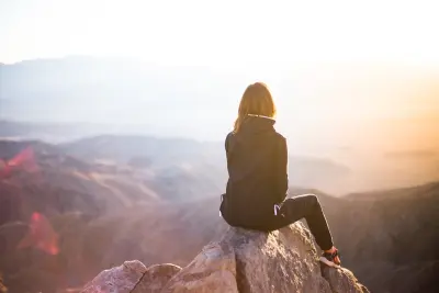 woman sitting on mountain peak looking out at sky