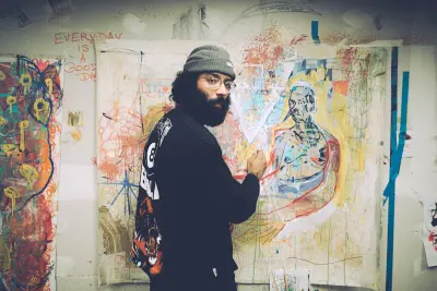man in standing beside wall, working on painting
