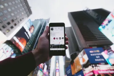 high angle photo of person holding turned on smartphone showing social media website with tall buildings background
