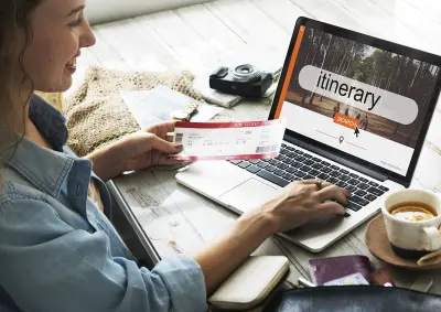 woman viewing a travel itinerary on a laptop while holding a ticket in one hand